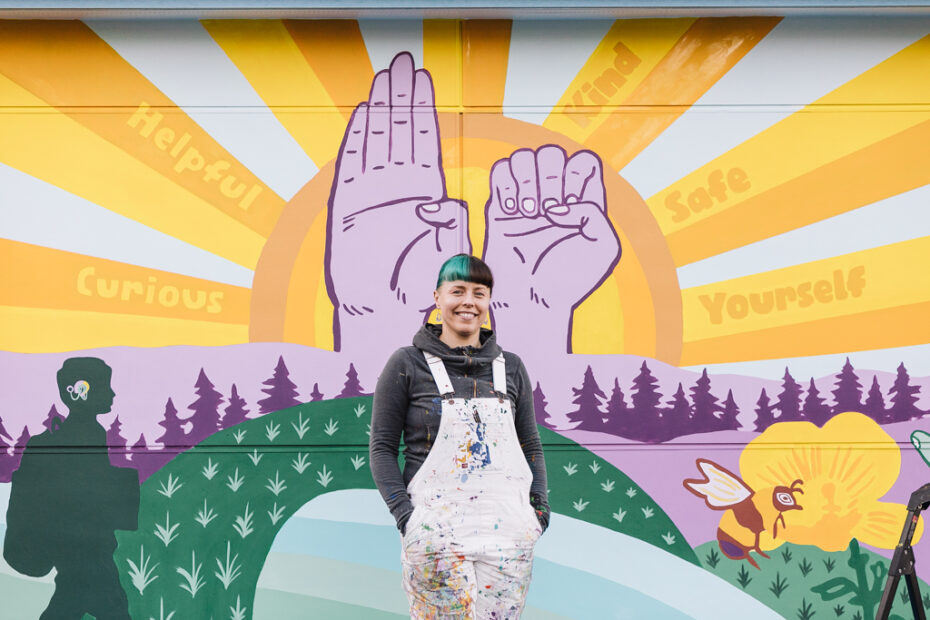 Artist Aistė Rye standing in front of a mural she designed for the Northwest School for Deaf and Hard-of-Hearing Children.